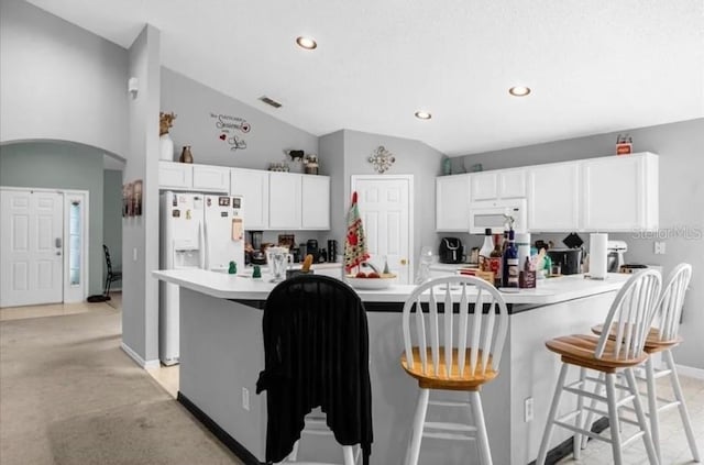 kitchen with light carpet, a breakfast bar, white appliances, vaulted ceiling, and white cabinets