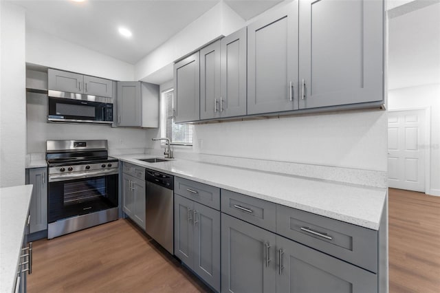 kitchen featuring sink, appliances with stainless steel finishes, gray cabinetry, dark hardwood / wood-style floors, and light stone counters