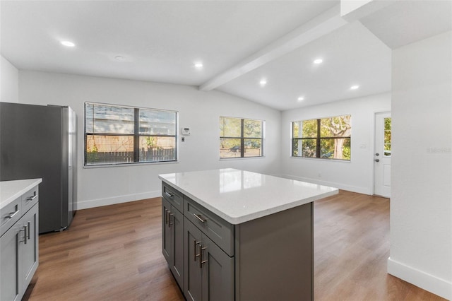 kitchen with vaulted ceiling with beams, hardwood / wood-style flooring, stainless steel fridge, and a kitchen island