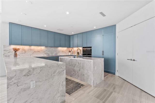 kitchen featuring tasteful backsplash, light stone counters, sink, blue cabinetry, and a kitchen island