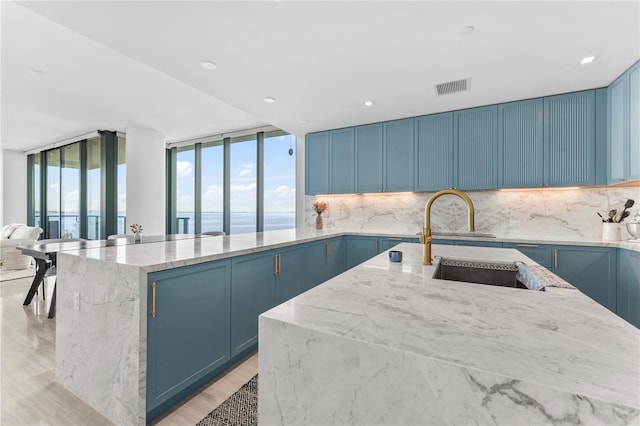 kitchen featuring decorative backsplash, light wood-type flooring, sink, a water view, and a kitchen island