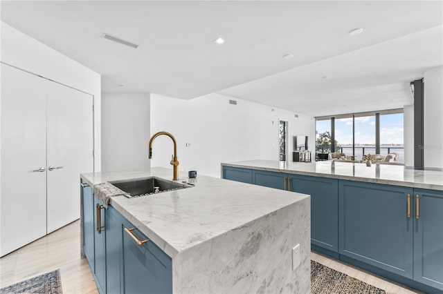 kitchen featuring light stone counters, a spacious island, blue cabinets, and sink