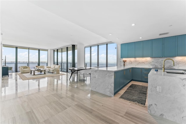 kitchen featuring sink, tasteful backsplash, expansive windows, blue cabinets, and a water view