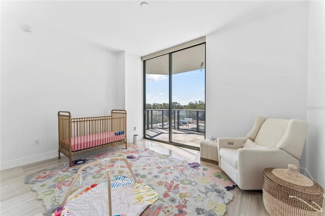 bedroom with access to exterior, light wood-type flooring, and floor to ceiling windows