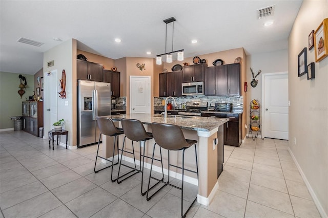 kitchen with pendant lighting, backsplash, an island with sink, dark brown cabinetry, and stainless steel appliances