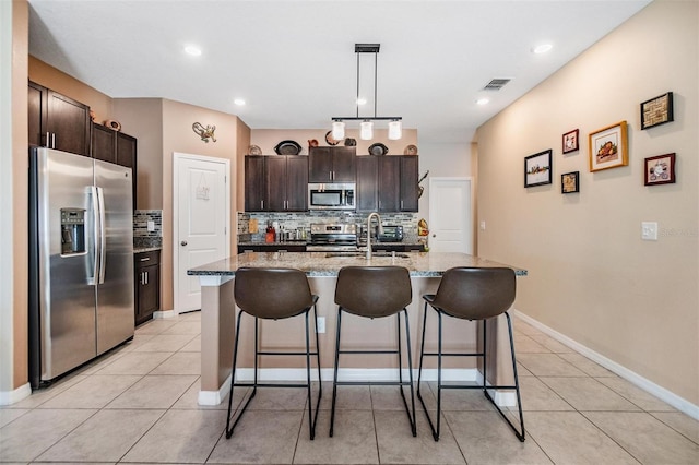 kitchen featuring sink, decorative backsplash, an island with sink, dark brown cabinetry, and stainless steel appliances