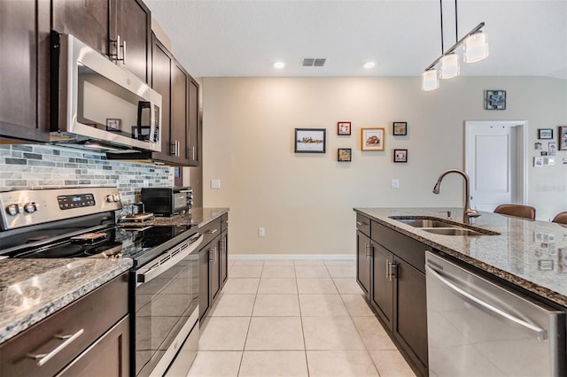 kitchen with sink, appliances with stainless steel finishes, decorative light fixtures, light stone counters, and dark brown cabinetry