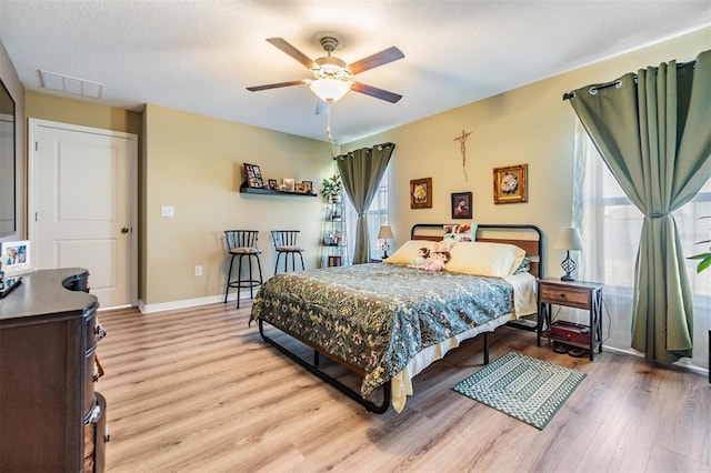 bedroom featuring ceiling fan, light hardwood / wood-style floors, a textured ceiling, and multiple windows