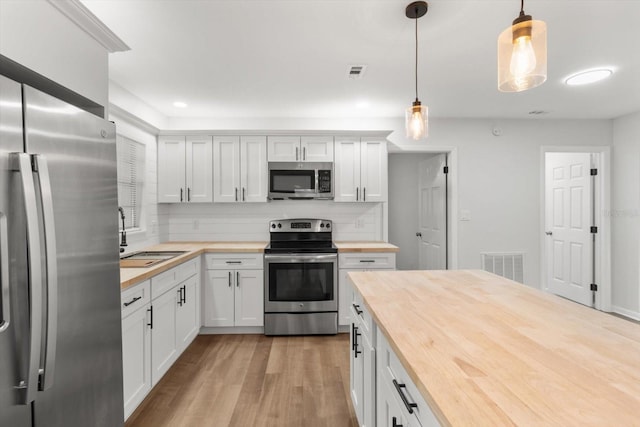 kitchen with white cabinets, pendant lighting, stainless steel appliances, and butcher block counters