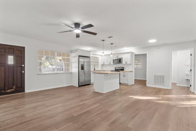 kitchen featuring light wood-type flooring, stainless steel appliances, decorative light fixtures, white cabinets, and a kitchen island