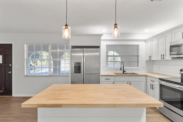 kitchen featuring white cabinets, light hardwood / wood-style floors, hanging light fixtures, and appliances with stainless steel finishes