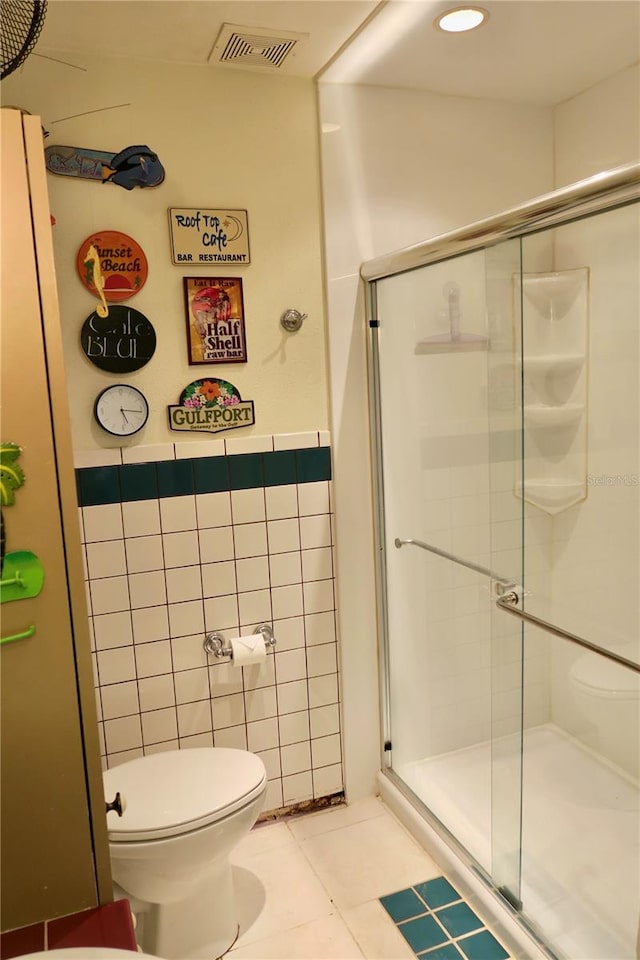 bathroom with toilet, tile patterned floors, walk in shower, and tile walls