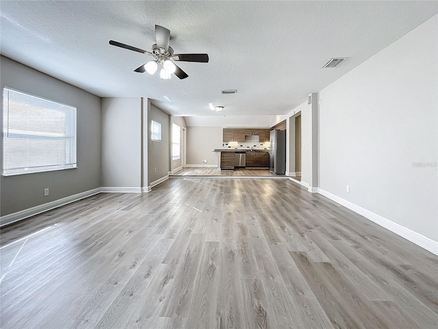 unfurnished living room featuring a textured ceiling, light hardwood / wood-style flooring, ceiling fan, and a healthy amount of sunlight