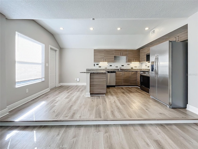 kitchen with appliances with stainless steel finishes, backsplash, light hardwood / wood-style floors, and lofted ceiling