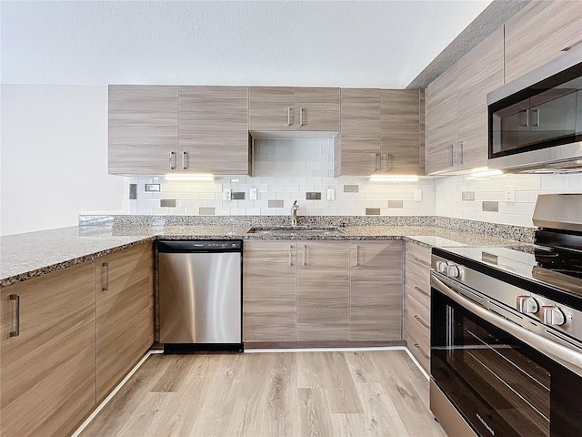 kitchen with sink, light stone counters, backsplash, light hardwood / wood-style floors, and appliances with stainless steel finishes