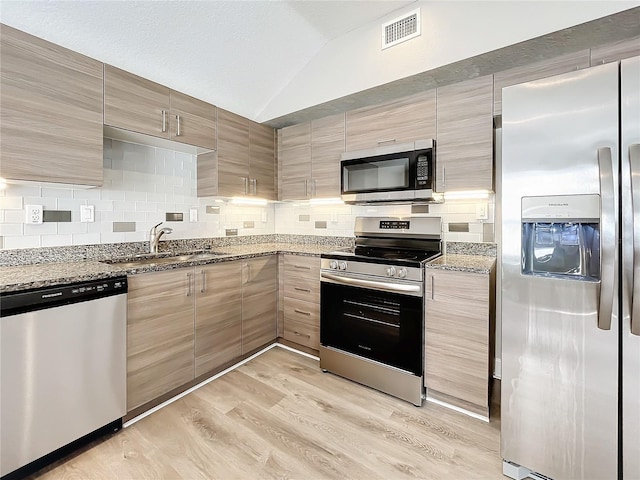 kitchen with light stone counters, stainless steel appliances, vaulted ceiling, sink, and light hardwood / wood-style flooring