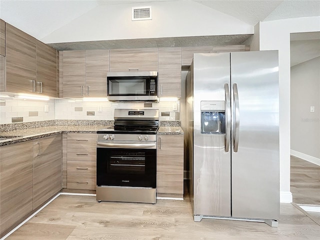 kitchen featuring stainless steel appliances, light hardwood / wood-style flooring, lofted ceiling, and stone countertops