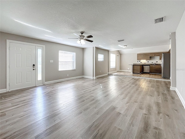 unfurnished living room with ceiling fan, light wood-type flooring, and a textured ceiling