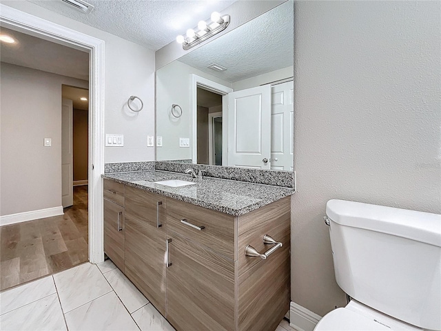 bathroom with hardwood / wood-style floors, vanity, toilet, and a textured ceiling