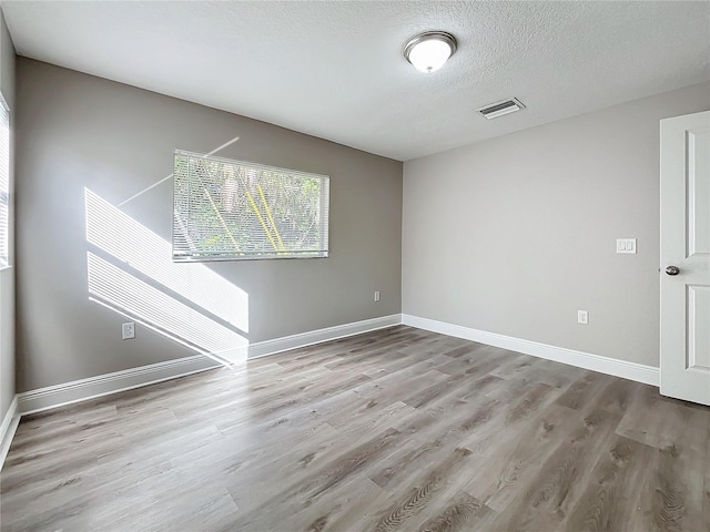 empty room with light wood-type flooring and a textured ceiling