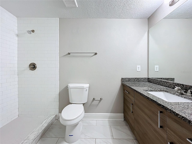 bathroom with a textured ceiling, vanity, toilet, and tiled shower