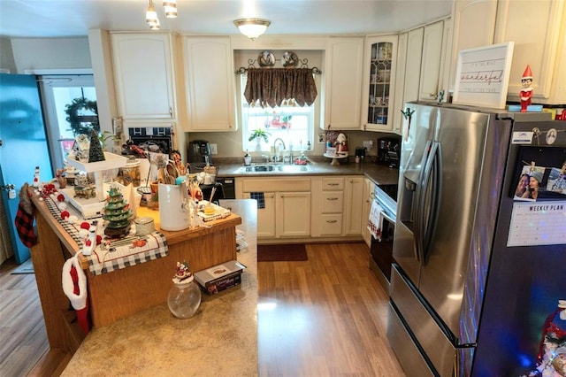 kitchen with stainless steel refrigerator with ice dispenser, light wood-type flooring, stove, sink, and white cabinetry