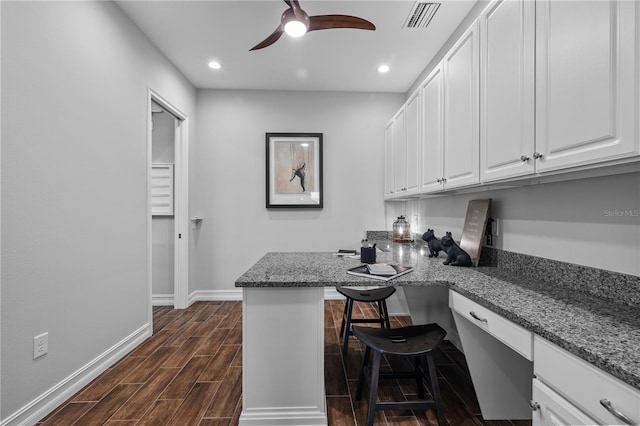 kitchen with dark hardwood / wood-style flooring, kitchen peninsula, a breakfast bar area, white cabinets, and built in desk