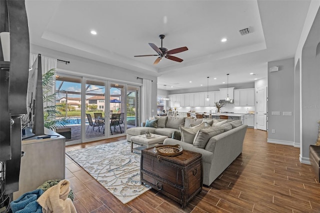 living room featuring ceiling fan, dark hardwood / wood-style flooring, and a tray ceiling