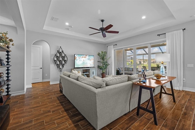 living room with ceiling fan, dark hardwood / wood-style flooring, and a tray ceiling