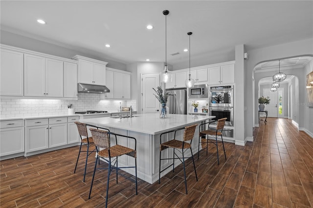 kitchen featuring a kitchen island with sink, dark wood-type flooring, stainless steel appliances, and ornamental molding