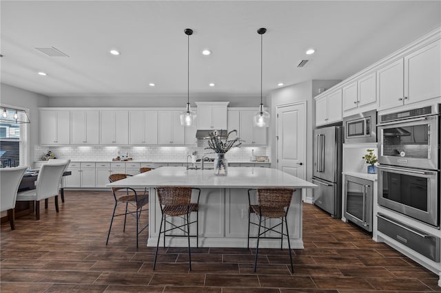 kitchen featuring pendant lighting, stainless steel appliances, white cabinetry, and an island with sink