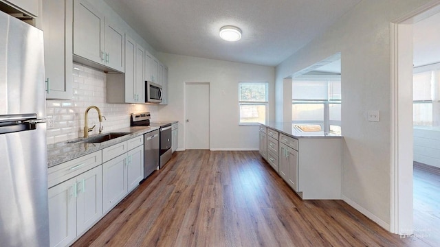 kitchen with sink, stainless steel appliances, light hardwood / wood-style flooring, backsplash, and vaulted ceiling