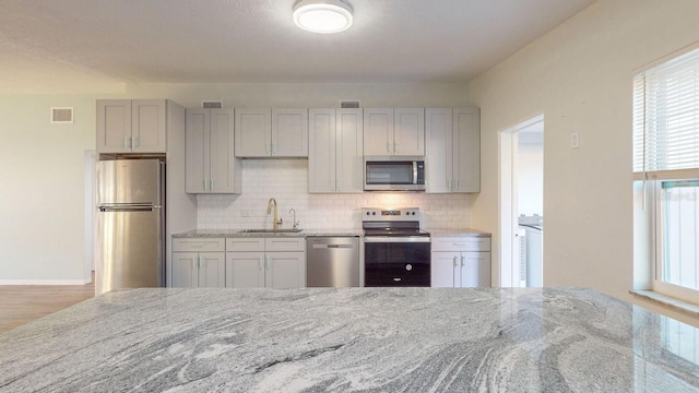 kitchen featuring a wealth of natural light, sink, stainless steel appliances, tasteful backsplash, and light stone counters