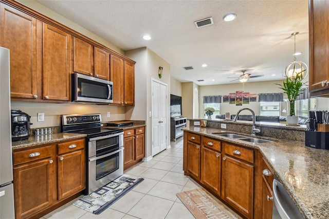 kitchen featuring sink, ceiling fan, dark stone countertops, a textured ceiling, and appliances with stainless steel finishes