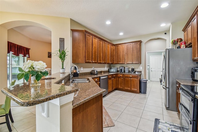 kitchen with a breakfast bar, dark stone counters, sink, kitchen peninsula, and stainless steel appliances