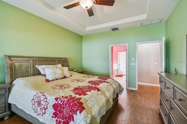 bedroom with dark hardwood / wood-style flooring, a tray ceiling, ensuite bath, and ceiling fan