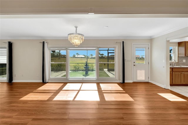 doorway to outside with light wood-type flooring, crown molding, a notable chandelier, and sink