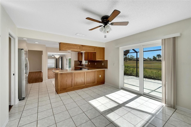 kitchen featuring ceiling fan, stainless steel fridge, a textured ceiling, light tile patterned flooring, and kitchen peninsula