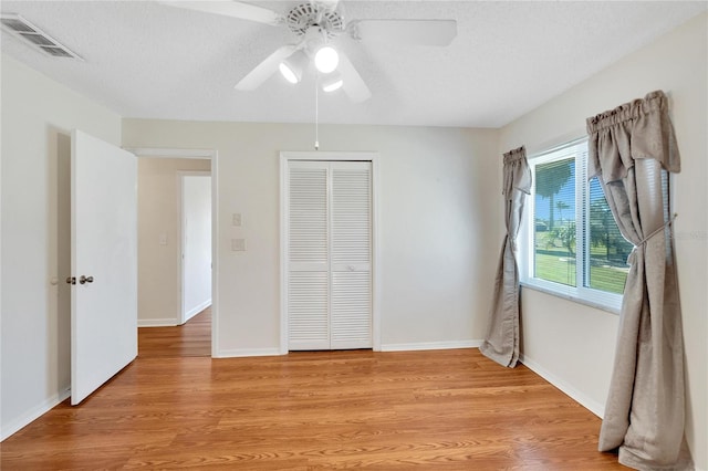 unfurnished bedroom with ceiling fan, a closet, light hardwood / wood-style floors, and a textured ceiling