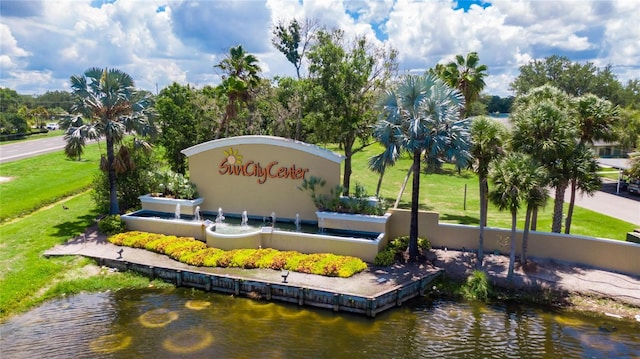 community / neighborhood sign featuring a water view and a lawn