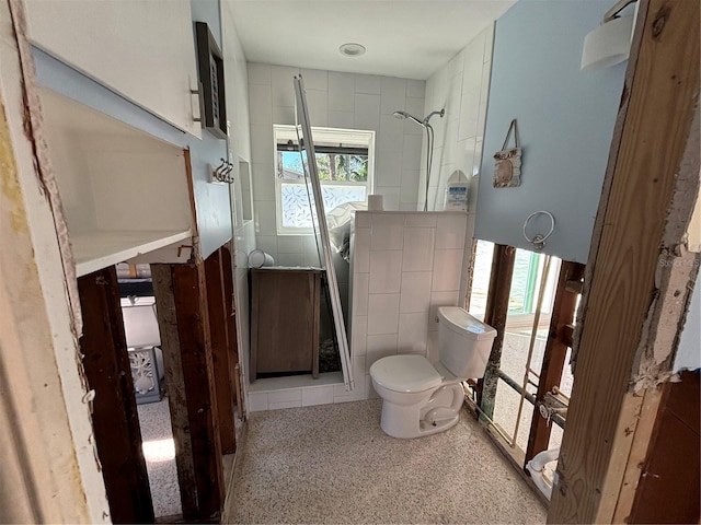 bathroom with a shower, toilet, a wealth of natural light, and tile walls