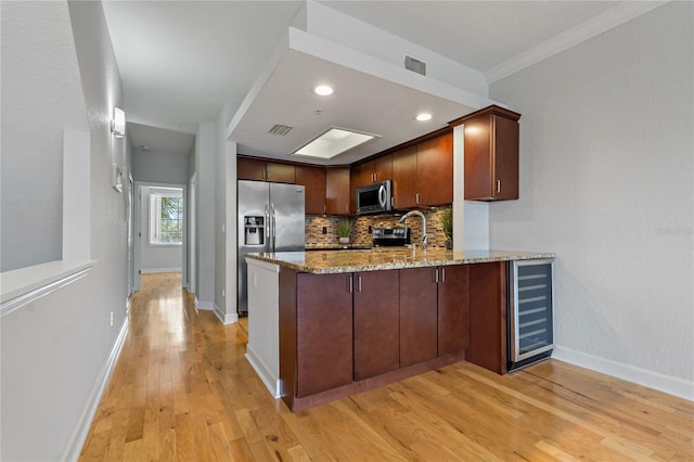 kitchen with light hardwood / wood-style flooring, light stone counters, kitchen peninsula, stainless steel appliances, and beverage cooler