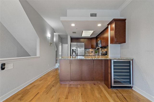 kitchen with kitchen peninsula, light stone counters, beverage cooler, and stainless steel appliances