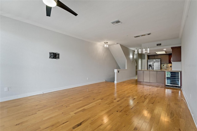 unfurnished living room with ceiling fan, light wood-type flooring, crown molding, and wine cooler