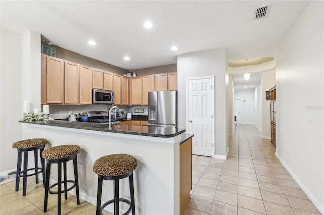 kitchen featuring kitchen peninsula, a kitchen breakfast bar, stainless steel appliances, and dark stone counters