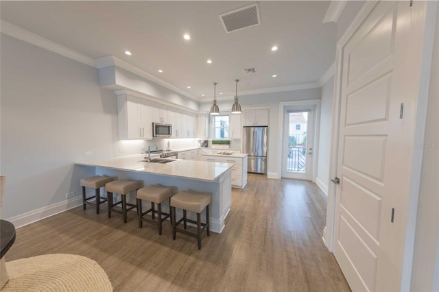 kitchen with white cabinets, appliances with stainless steel finishes, decorative light fixtures, sink, and kitchen peninsula