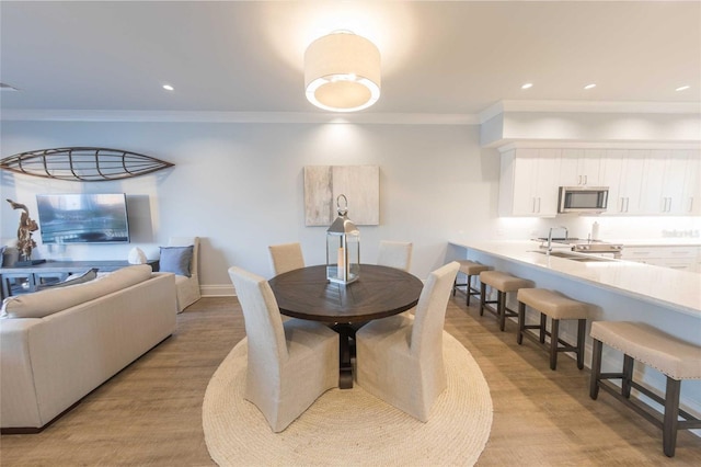 dining space featuring light wood-type flooring, sink, and ornamental molding