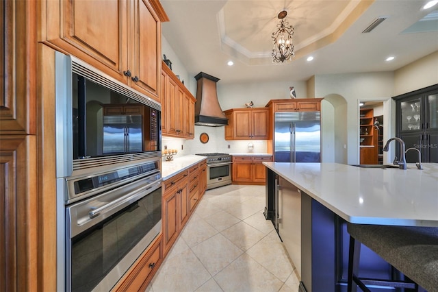 kitchen featuring custom exhaust hood, premium appliances, a large island, a raised ceiling, and a breakfast bar