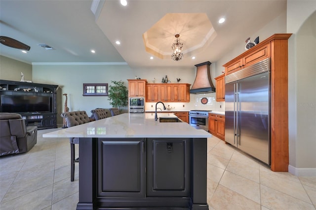 kitchen featuring premium range hood, a large island with sink, a breakfast bar area, and built in appliances