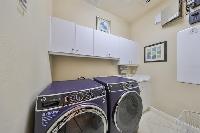 clothes washing area with washer and clothes dryer, light tile patterned floors, and cabinets